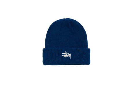 A dark blue ribbed knit beanie hat with a folded cuff and a white embroidered Stüssy logo on the front, set against a plain white background.