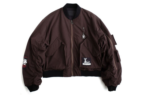 A dark brown nylon bomber jacket with black ribbed trim, featuring a front zipper, zippered chest pocket, and embroidered patches on the sleeves and chest.