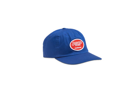 A royal blue baseball cap with a curved brim, featuring a circular red and white embroidered patch on the front that reads 'SERVICE WORK uniform'. The cap is photographed on a clean white background.
