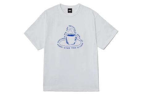 A white short-sleeve crewneck t-shirt featuring a blue graphic print of a coffee cup and saucer with circular text, displayed flat against a white background.