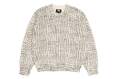 A knit crewneck sweater featuring a black and off-white grid-like pattern, laid flat against a solid white background. A black brand label is visible at the inner collar.