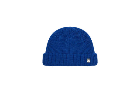 A royal blue ribbed knit beanie hat with a small white square logo patch on the front of the folded cuff, shown against a plain white background.
