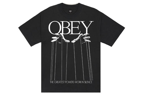 A black short-sleeve graphic t-shirt featuring the word 'OBEY' in large white letters, with illustrated puppet strings and hands beneath it, and the phrase 'THE GREATEST POWERS WORN IN SILENCE' printed at the bottom.