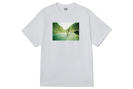 White t-shirt with a graphic of a person running on a road with green hills.
