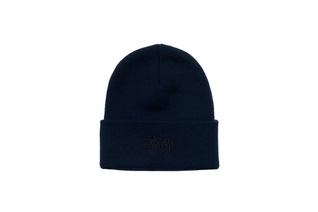 A dark navy blue knit beanie hat with a folded cuff, featuring a tonal embroidered Stüssy logo on the front, set against a plain white background.