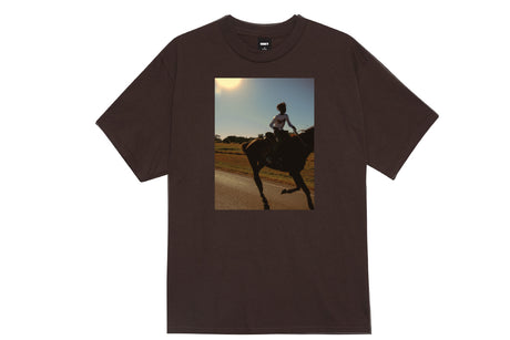 A dark brown short-sleeve t-shirt with a rectangular graphic print on the front showing a silhouette of a person riding a horse on a road at sunset.