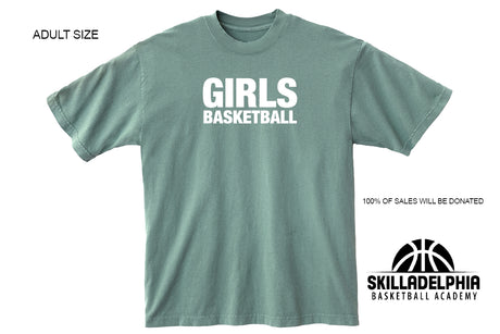 A sage green short-sleeve t-shirt with 'GIRLS BASKETBALL' printed in white across the chest. The image includes text overlays indicating 'ADULT SIZE' and '100% OF SALES WILL BE DONATED' along with the 'SKILLADELPHIA BASKETBALL ACADEMY' logo in the bottom right corner.