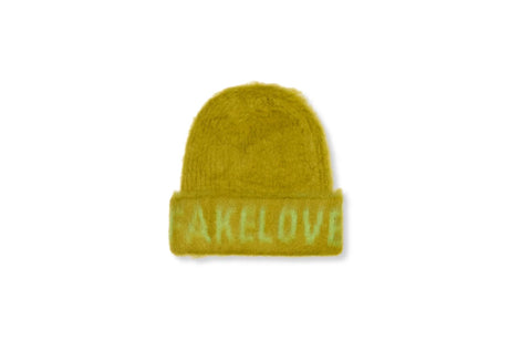 A fuzzy knit beanie hat in a mustard yellow color, featuring the word 'FAKELOVE' embroidered across the folded cuff in a lighter yellow-green thread, set against a plain white background.