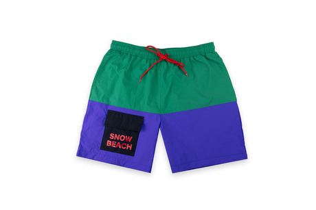 A pair of Snow Beach branded board shorts with a green upper half and blue lower half, featuring a drawstring waist, side pockets, and red embroidery on the front left leg.