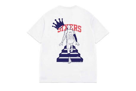 A white short-sleeve t-shirt shown from the back, featuring a graphic of a basketball player walking up steps under the word 'SIXTERS' in red with a navy blue crown above.
